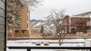 A view from a balcony with a wooden fence, snow-covered ground, and buildings in the background.