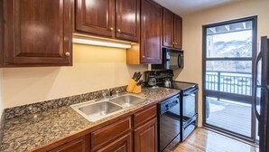 A kitchen with granite countertops, wooden cabinets, a stainless steel sink, a coffee maker, and a refrigerator.