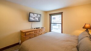A bedroom with a bed, a dresser, a television mounted on the wall, and a window with a view of the outside.