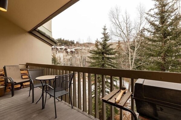 A balcony with a view of a forested area, a table with chairs, and a grill. - Townsend Place Ski-In Ski-Out Access Condo by RedAwning (Avon)