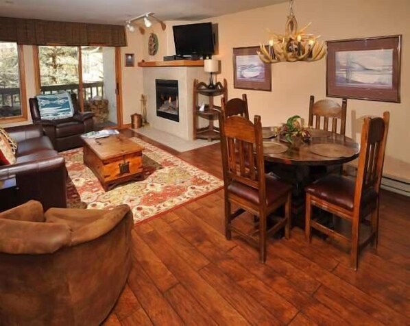 A cozy living room with a fireplace, a television, and a dining area with wooden furniture. - Townsend Place Ski-In Ski-Out Access Condo by RedAwning (Avon)