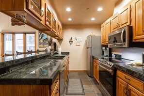 Una cocina con armarios de madera, encimera de granito, electrodomésticos de acero inoxidable y una ventana que deja entrar luz natural.