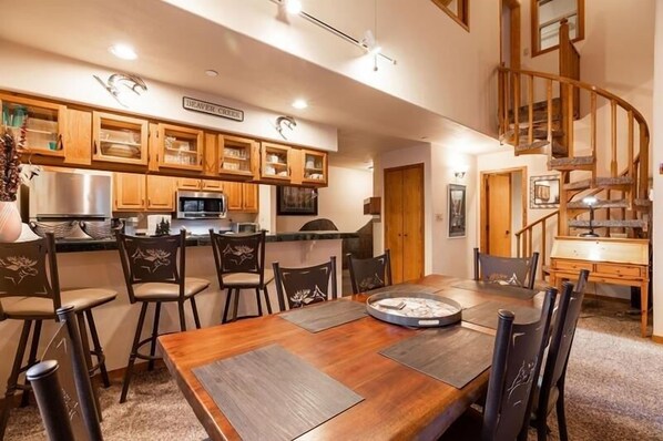 Una cocina amplia con armarios de madera, un comedor con una mesa grande y una escalera de madera.