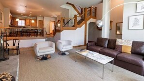 A spacious living area with a modern staircase, a sofa, a coffee table, and a dining area with wooden furniture. - Ski-in Ski-out Townhome in Beaver Creek by RedAwning (Avon)