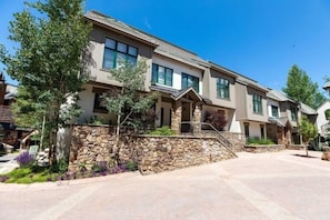 A modern multi-story residential building with a stone facade, large windows, and a well-maintained garden. - Ski-in Ski-out Townhome in Beaver Creek by RedAwning (Avon)