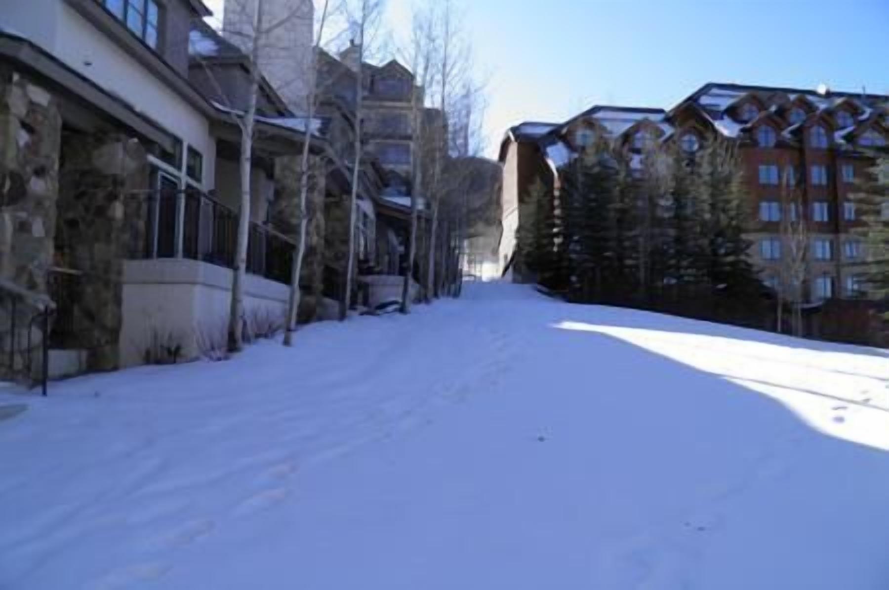 A snow-covered street with buildings on either side, including a multi-story building with a red facade and a stone building with a balcony.