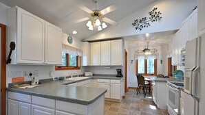 A kitchen with white cabinets, a granite countertop, a ceiling fan, and a chandelier.