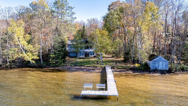 A lakeside cabin with a dock extending into the water, surrounded by autumn-colored trees.
