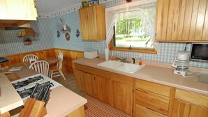 A kitchen with wooden cabinets, a sink, a stove, and a window with a view of trees. - Ranch-Style Seidls Home Feet away to Lakeshore by RedAwning (Cable)