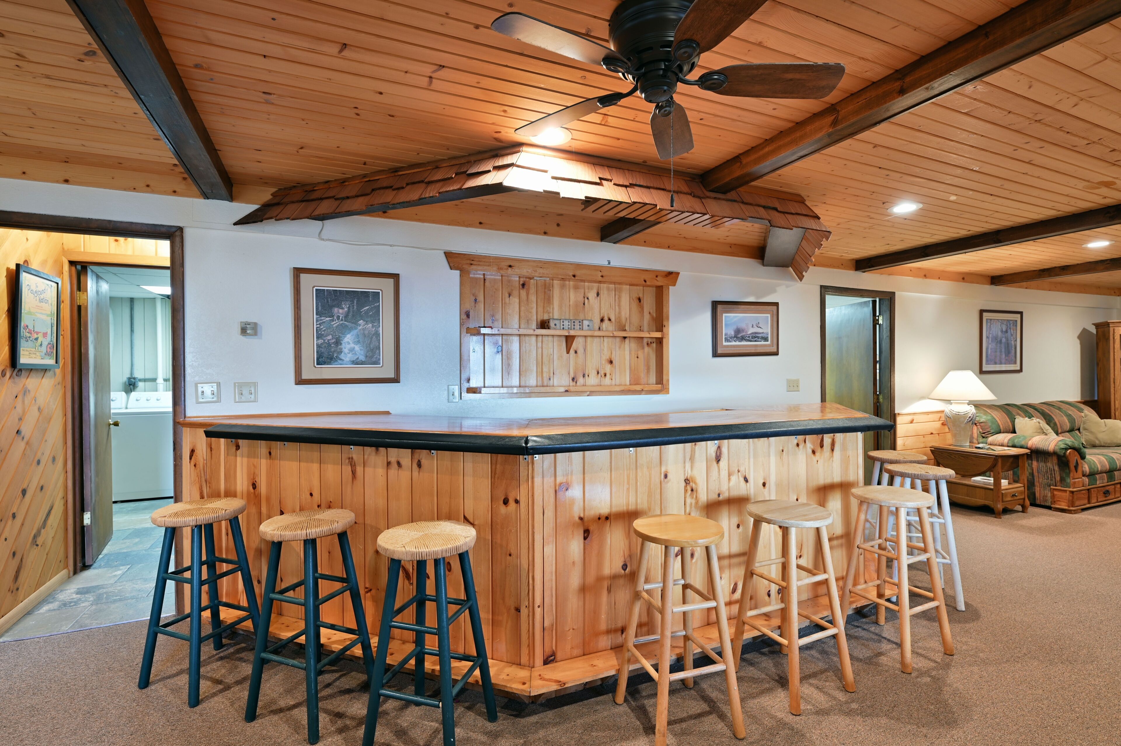 Una zona de bar con barra de madera, taburetes, ventilador de techo y encimera de cocina.