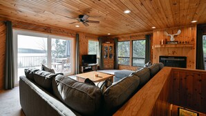 Ein gemütliches Blockhaus-Interieur mit Holzbalkendecke, einer großen Couch, einem Fernseher und einem Kamin.