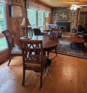 A cozy living room with a stone fireplace, wooden furniture, and a large window offering a view of the outdoors. - Butler's Bay Teal Lake 4 Bedroom Hotel Room by RedAwning (Hayward)