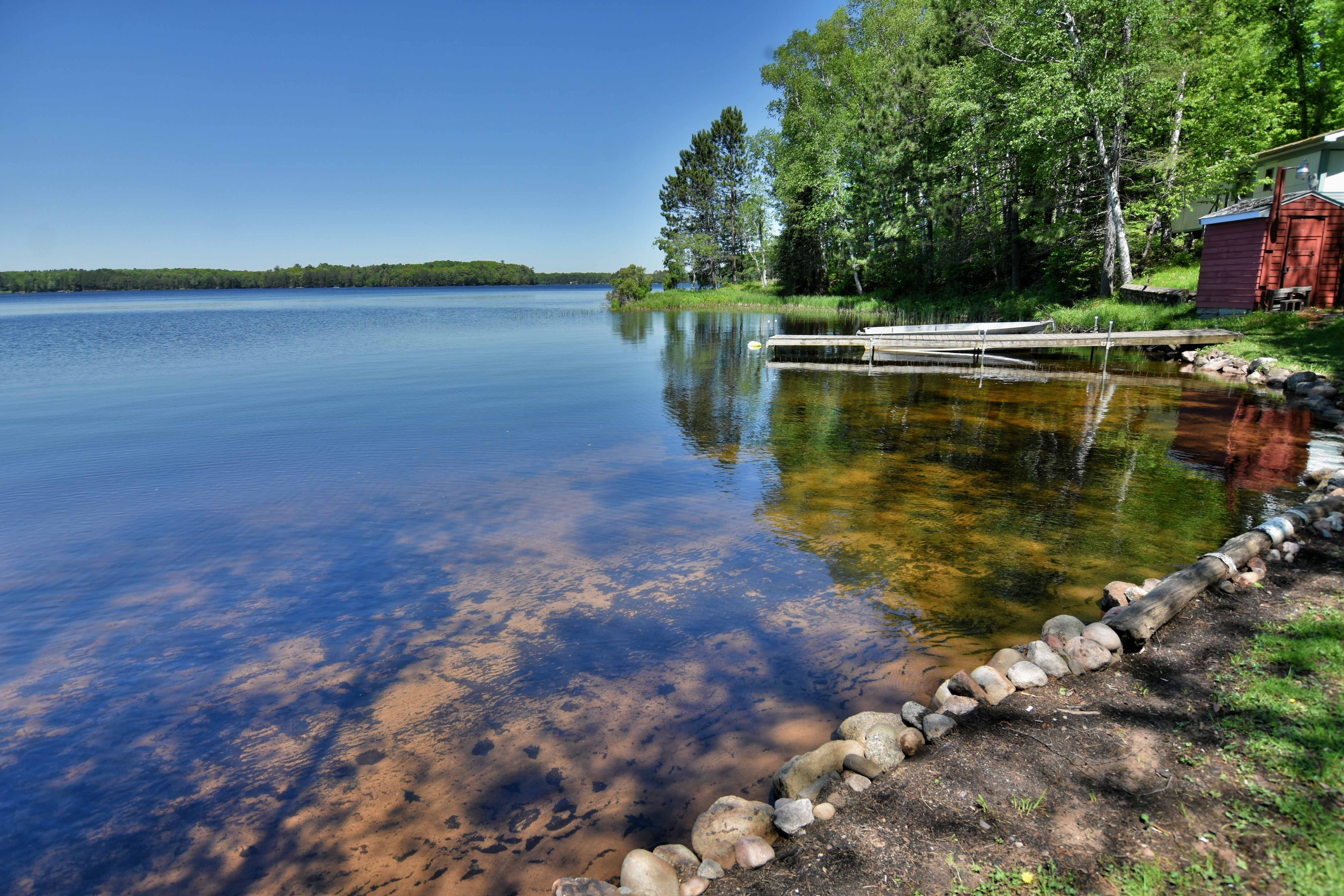 A calm lake with a dock, surrounded by trees and a small red building.