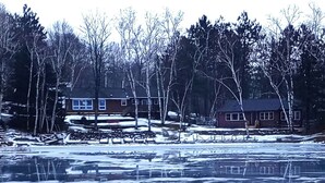 A frozen lake with reflections of houses and trees. - Butler's Bay Teal Lake 4 Bedroom Hotel Room by RedAwning (Hayward)