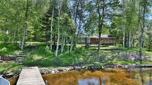 A wooden dock leading to a calm lake with a house in the background surrounded by trees. - Butler's Bay Teal Lake 4 Bedroom Hotel Room by RedAwning (Hayward)