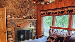 A cozy bedroom with a stone wall, a fireplace, a bed with animal-themed pillows, and a chandelier. - Butler's Bay Teal Lake 4 Bedroom Hotel Room by RedAwning (Hayward)