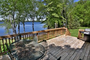 A wooden deck with a metal table and chairs, overlooking a lake with trees and a grassy area. - Butler's Bay Teal Lake 4 Bedroom Hotel Room by RedAwning (Hayward)
