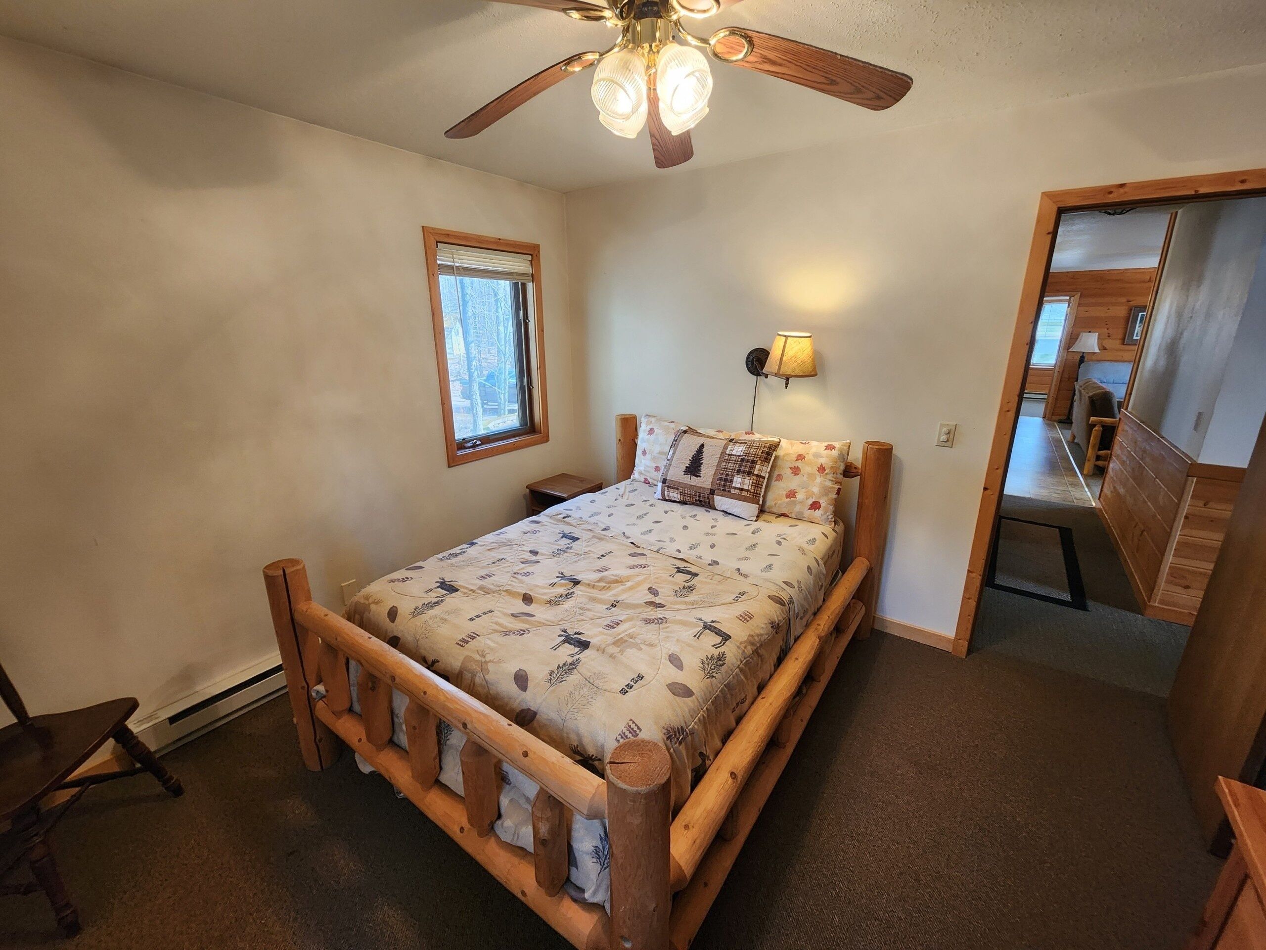 A bedroom with a wooden bed frame, a ceiling fan, a window, and a nightstand.