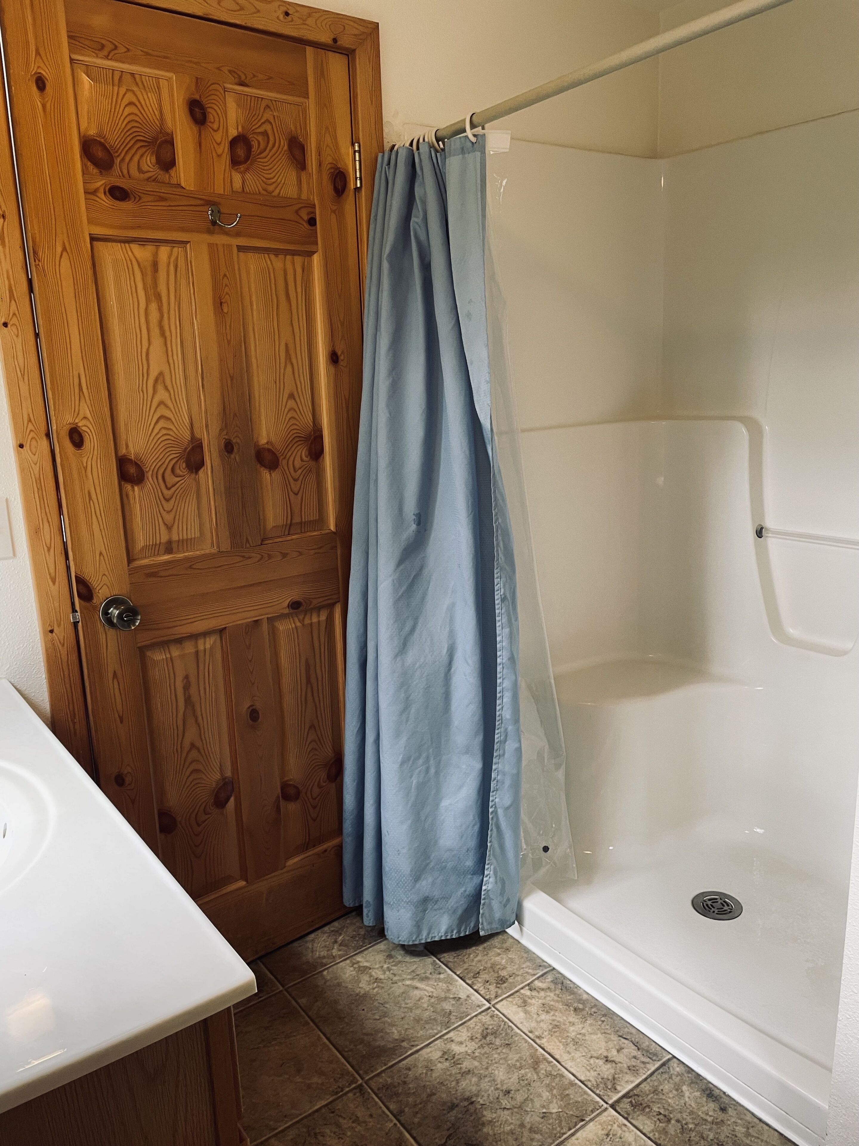 A bathroom with a wooden door, a shower with a clear glass door, and a white sink.