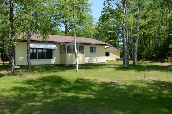 A yellow single-story house with a brown roof, surrounded by trees and grass.