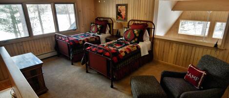 A cozy cabin room with two beds, a chair, a bench, and a wooden desk.