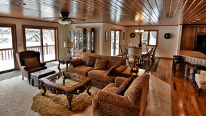 A spacious living room with a wooden ceiling, large windows, and a dining area.