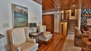 A spacious living room with a wooden ceiling, a stone wall, and a staircase leading to an upper level.