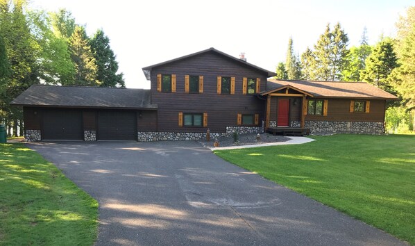 A two-story house with a stone foundation, a garage, and a covered porch. - Peace Of Mind On Namakagon 5 Bedroom Hotel Room by RedAwning (Cable)
