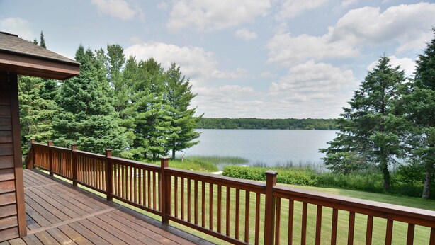 A wooden deck with a railing overlooking a lake and forest.