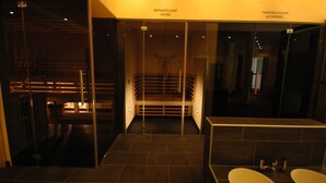 A modern bathroom with a glass enclosure leading to a sauna area, a separate shower area, and a sink with a mirror. - Das Moerisch (Seeboden)