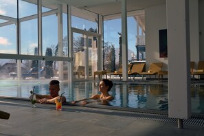 A swimming pool with clear glass walls, lounge chairs, and a view of the outside. - Das Moerisch (Seeboden)