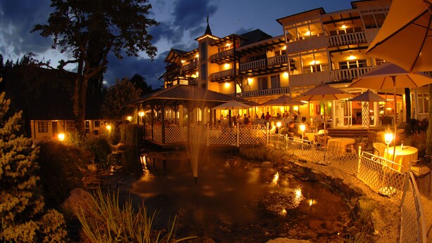 A large hotel with multiple balconies, outdoor seating, and a pond. - Das Moerisch (Seeboden)