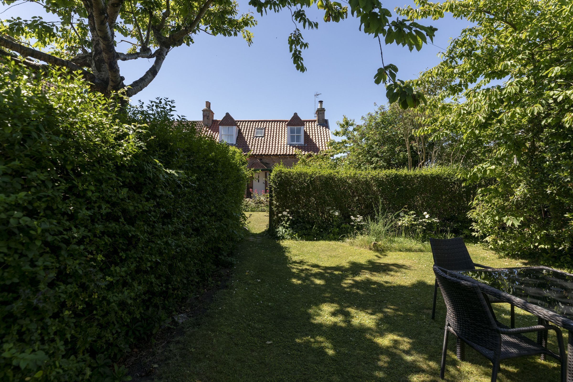 A garden pathway leading to a house with a red-tiled roof and dormer windows.