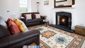 A living room with a fireplace, two sofas, a patterned rug, and a window. - WINDYRIG, Cockburnspath - sleeps 4 in 2 bedrooms (Cockburnspath)