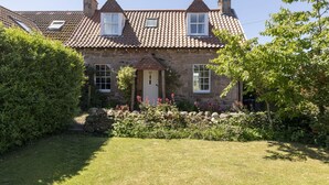 A stone house with a tiled roof, a front door, and a small garden with shrubs and flowers. - WINDYRIG, Cockburnspath - sleeps 4 in 2 bedrooms (Cockburnspath)