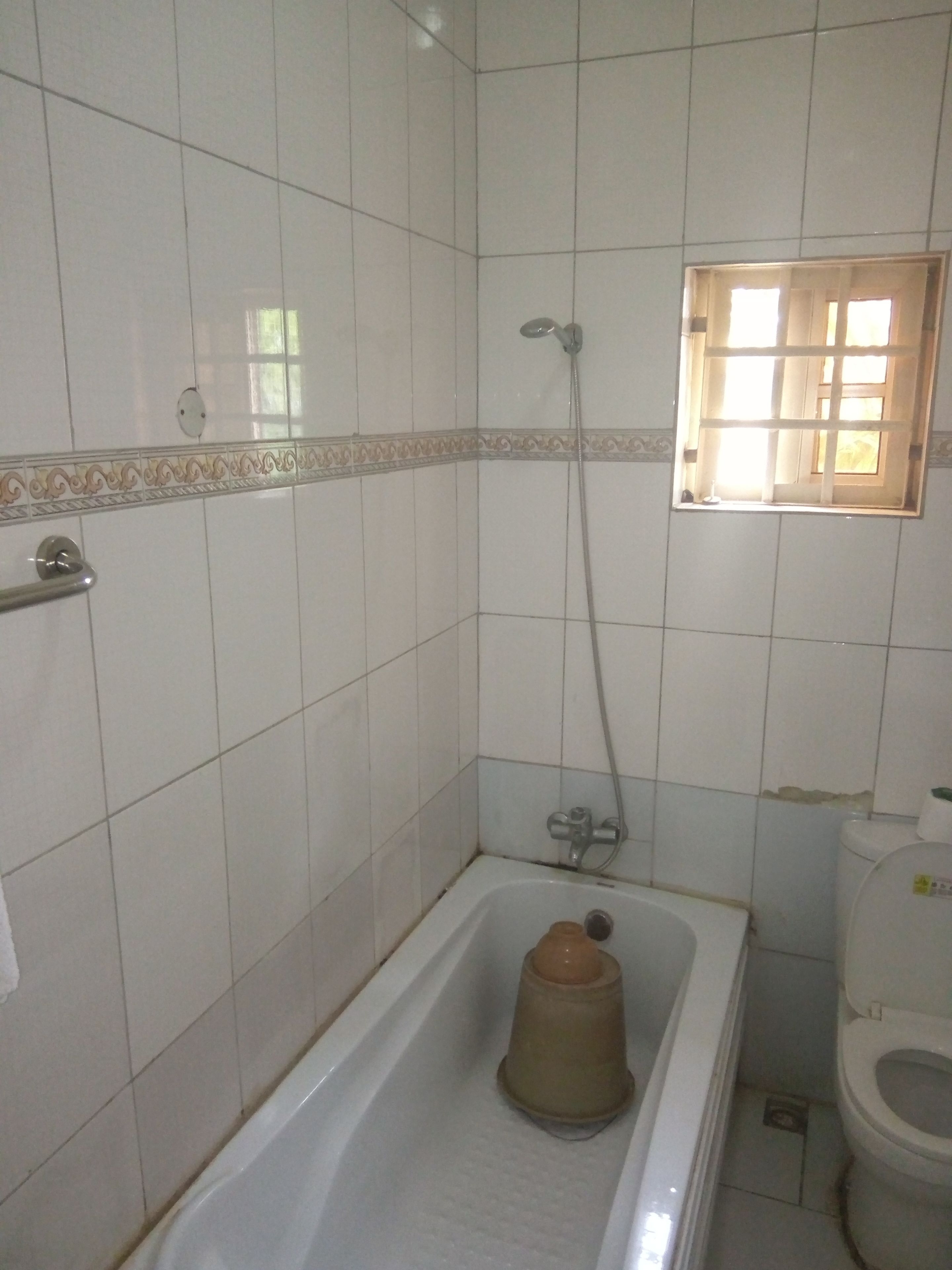 Une salle de bain avec des murs recouverts de carreaux blancs, une baignoire, une douche et des toilettes.
