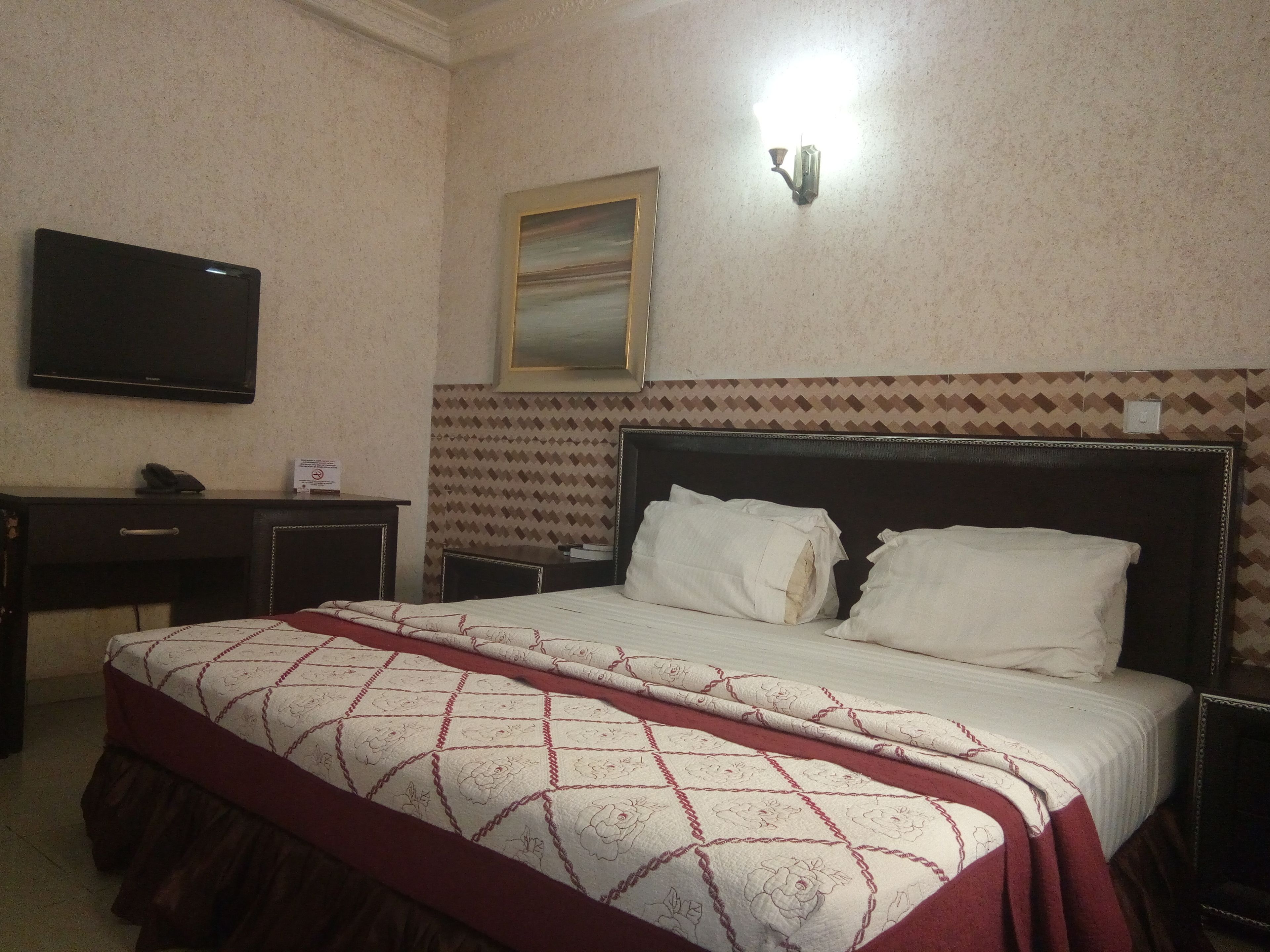 Una habitación de hotel con una cama, un escritorio, una silla, un televisor y una lámpara fijada a la pared.
