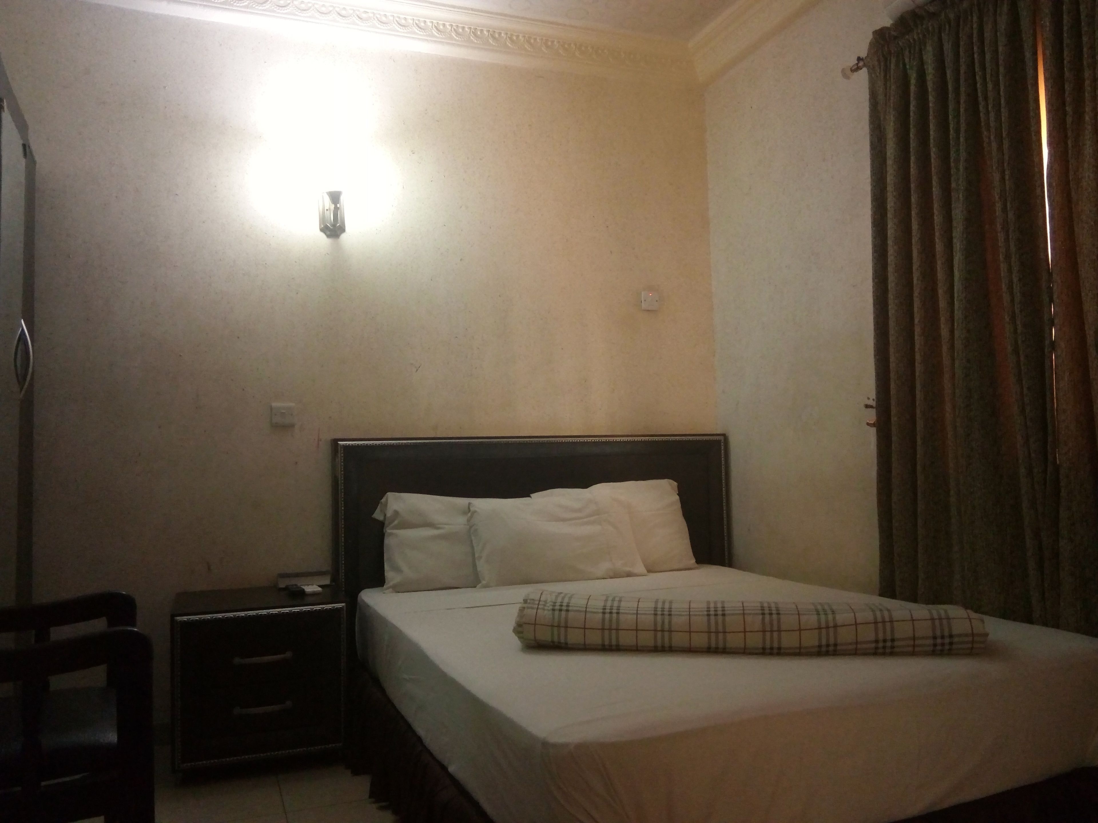 A bedroom with a bed, a nightstand, a lamp, and a curtain.