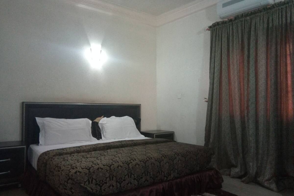 Une chambre à coucher comprenant un lit, une table de chevet, un climatiseur fixé au mur et un rideau.
