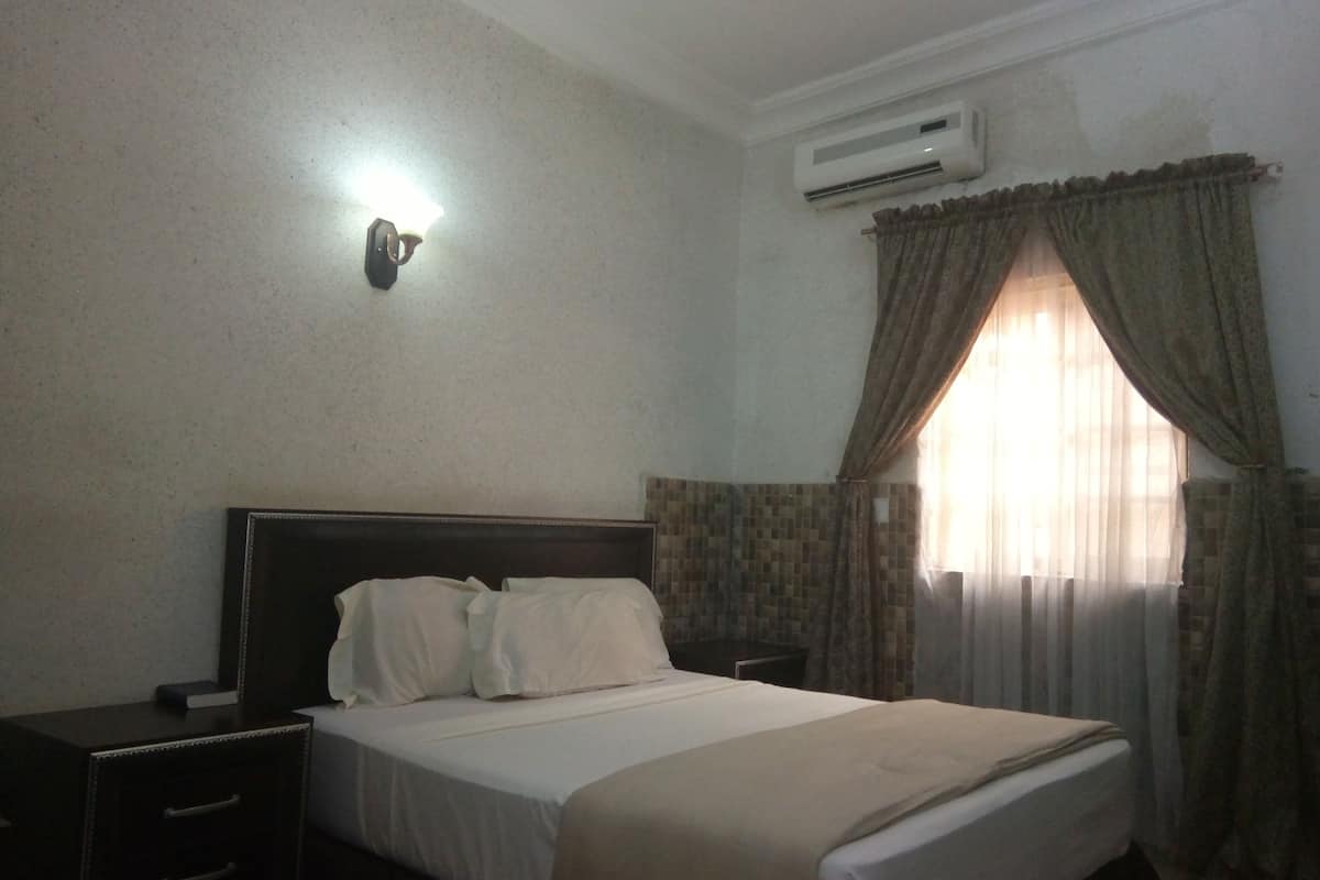 Une chambre d’hôtel équipée d’un lit, d’une table de chevet, d’un climatiseur fixé au mur et d’une fenêtre avec des rideaux.