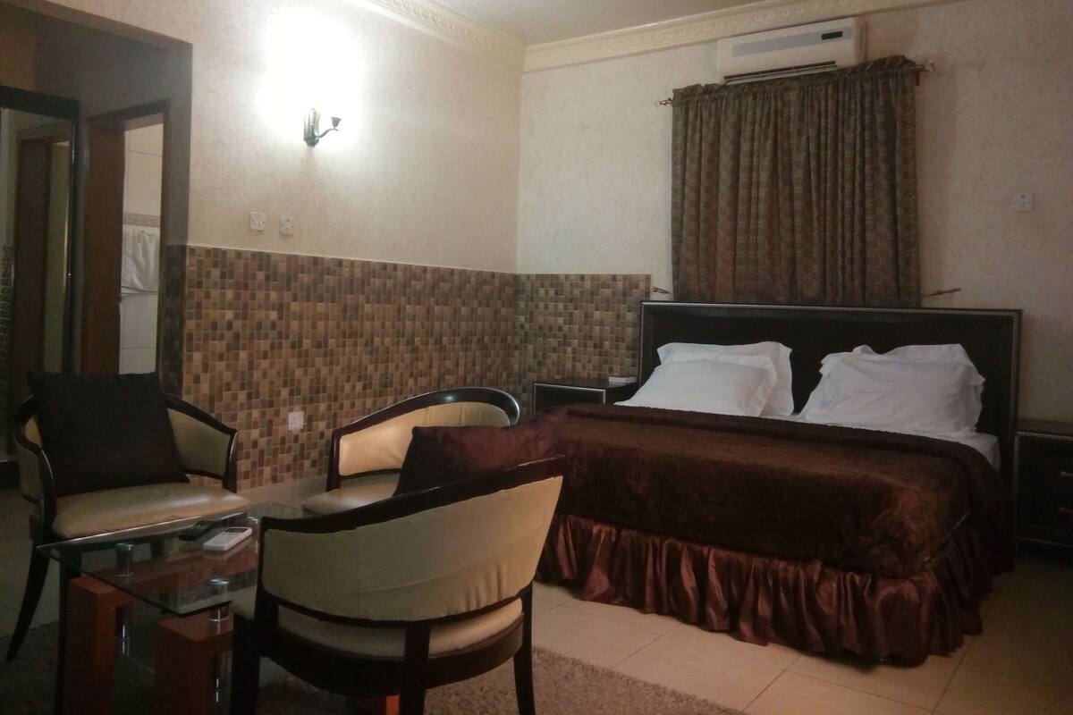 Une chambre d’hôtel avec un lit, deux chaises, une petite table et un climatiseur fixé au mur.