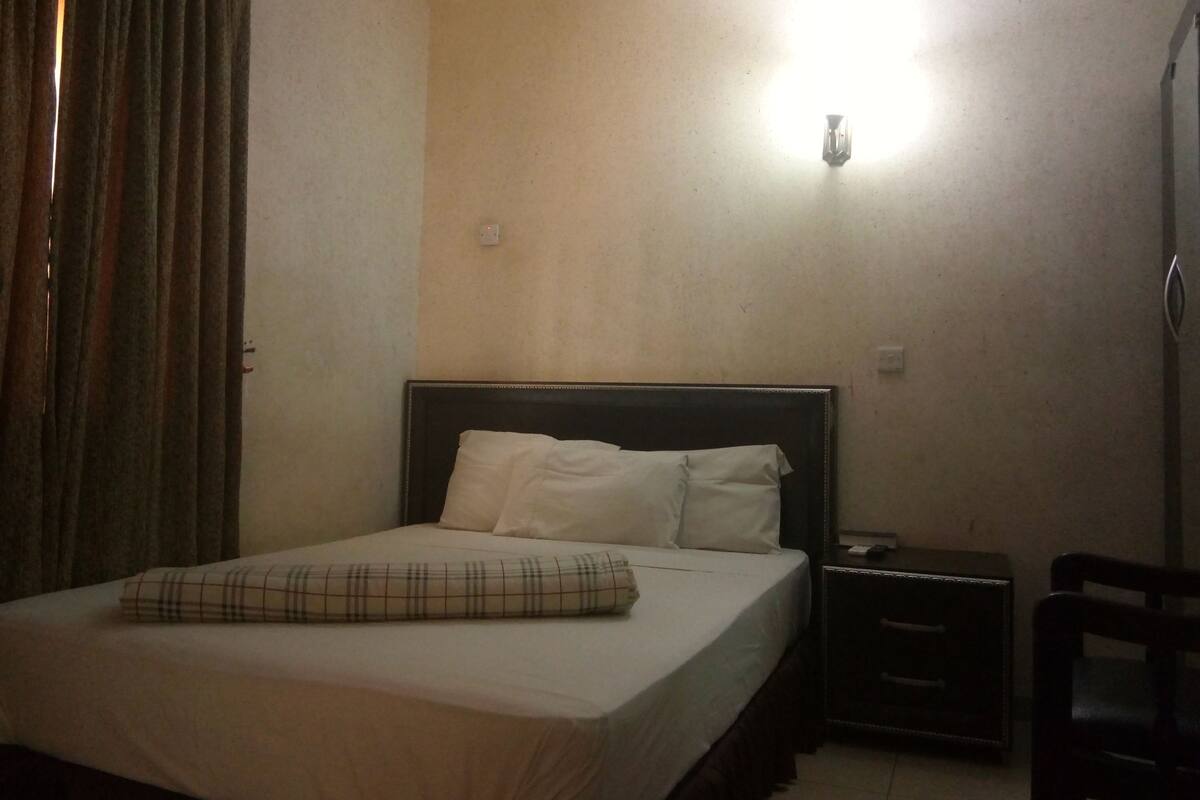Une chambre d’hôtel comprenant un lit, une table de chevet, une chaise et une lampe fixée au mur.