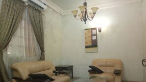 A living room with two beige leather sofas, a glass coffee table, a chandelier, and a wall-mounted artwork. - Rila Muam Castle Hotel (Kaduna)