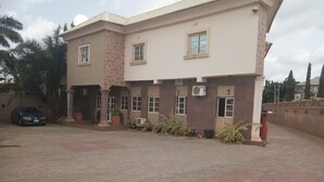 A two-story building with a brick facade, multiple windows, and a paved driveway. - Rila Muam Castle Hotel (Kaduna)