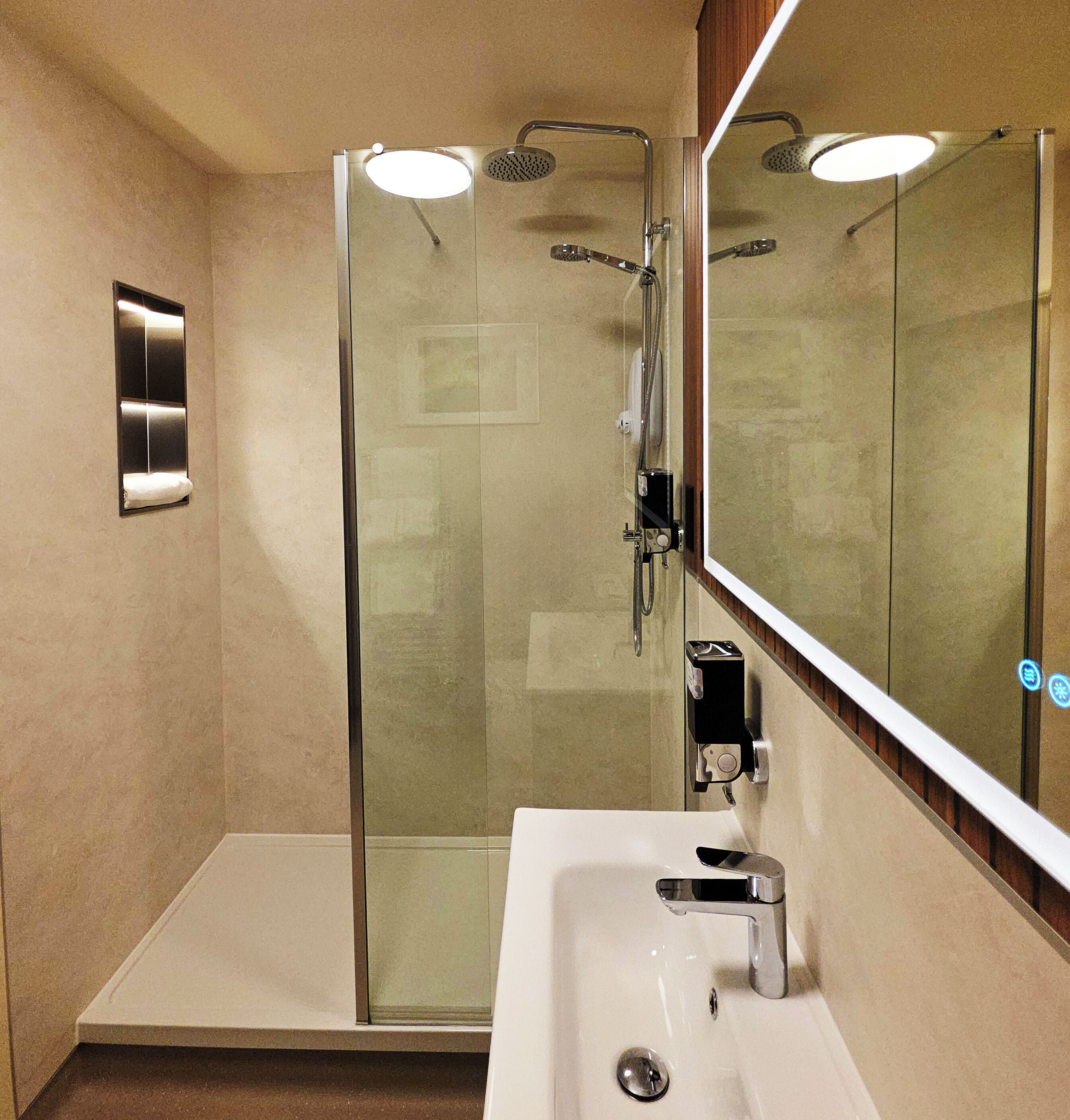 Un baño moderno con ducha acristalada, lavamanos y espejo.