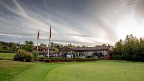 A golf course with a clubhouse, flags, and a clear sky. - The Dorset Golf Hotel (Wareham)