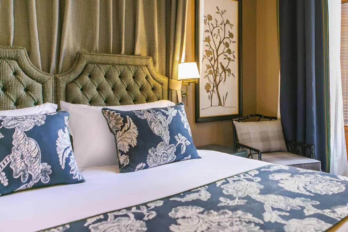 A hotel room with a large bed, a chair, a lamp, and a painting on the wall.