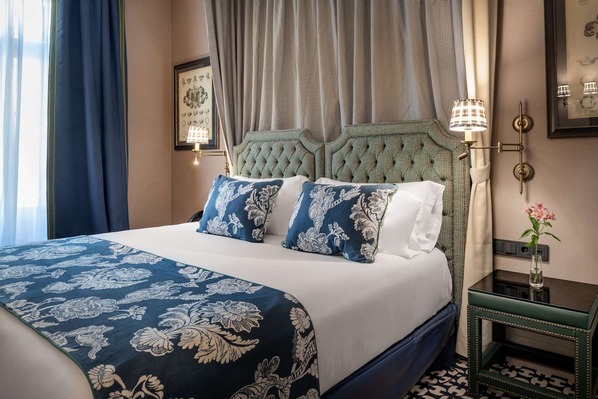 A neatly made bed with a floral bedspread, a headboard with a tufted design, and a bedside table with a lamp.