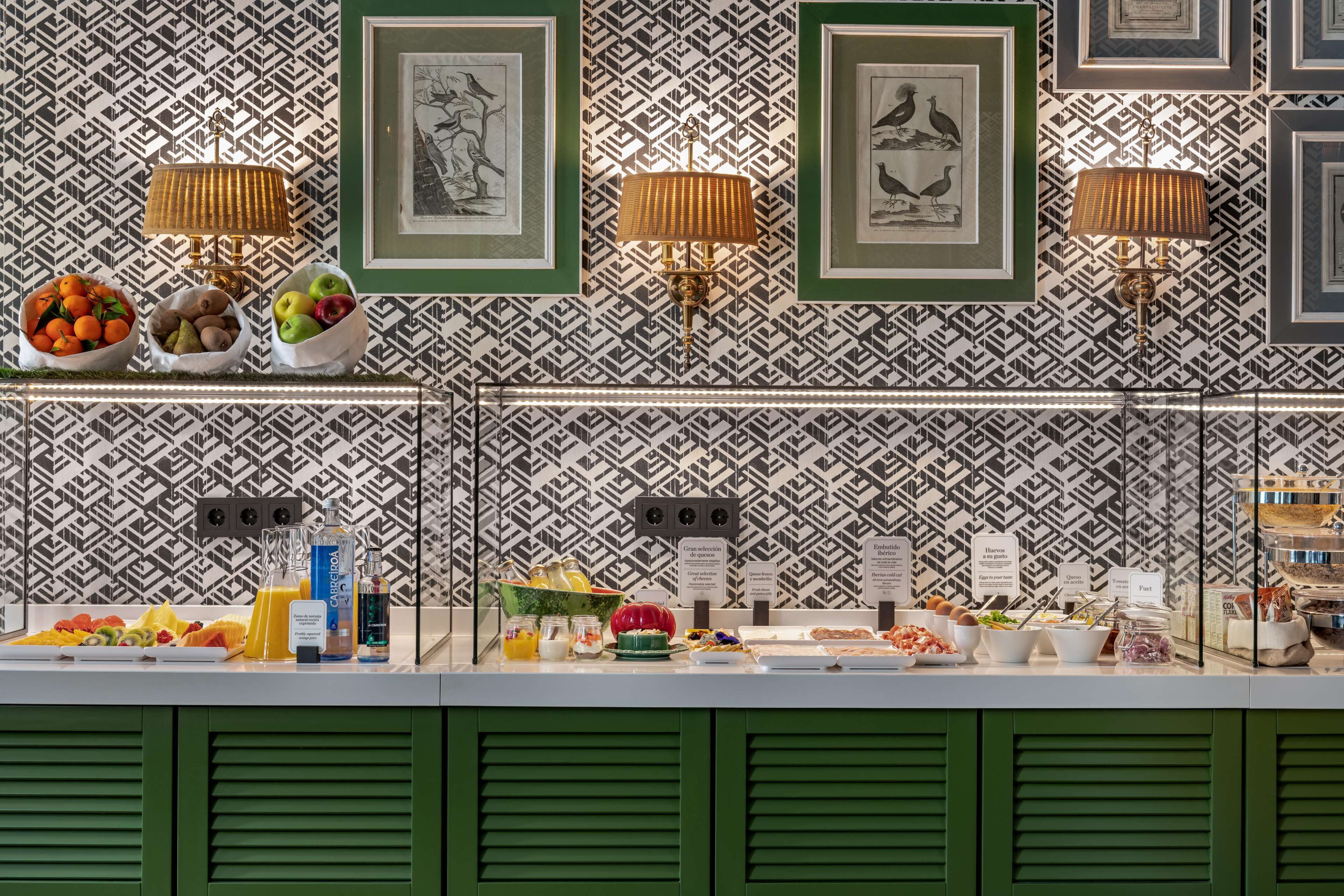A buffet with various food items and a patterned wall with framed pictures.