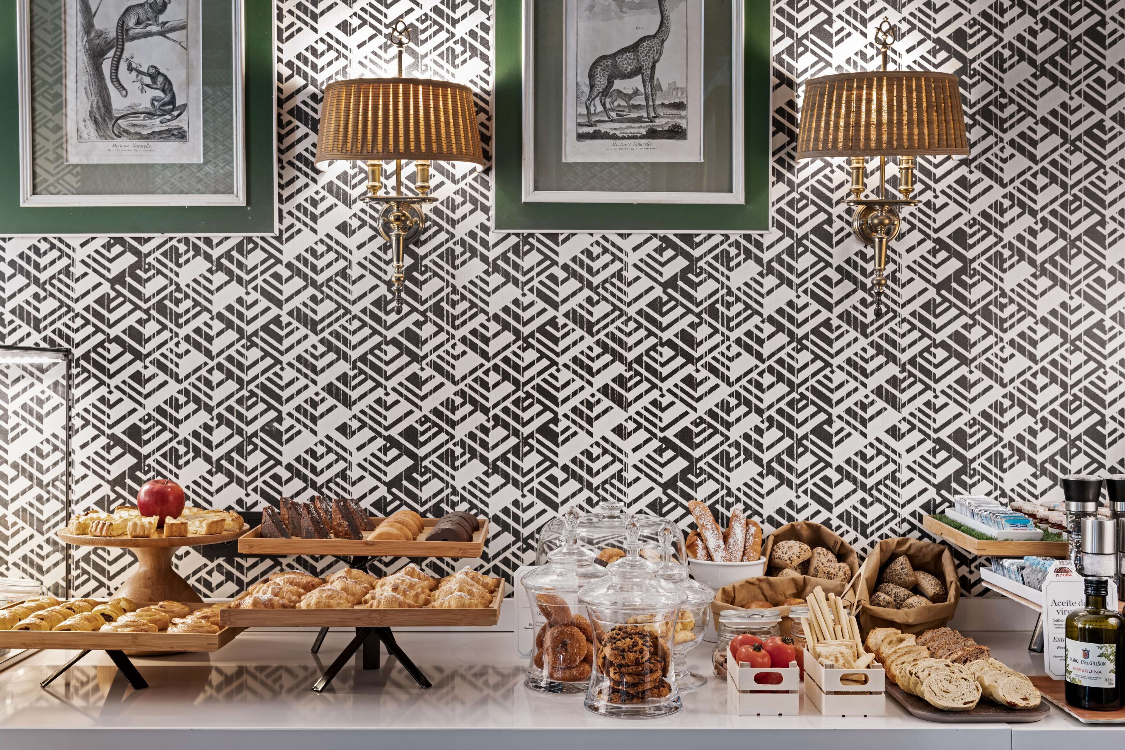Un buffet proposant une variété de viennoiseries et de pains, disposé devant un papier peint à motifs, orné d’illustrations d’animaux encadrées.